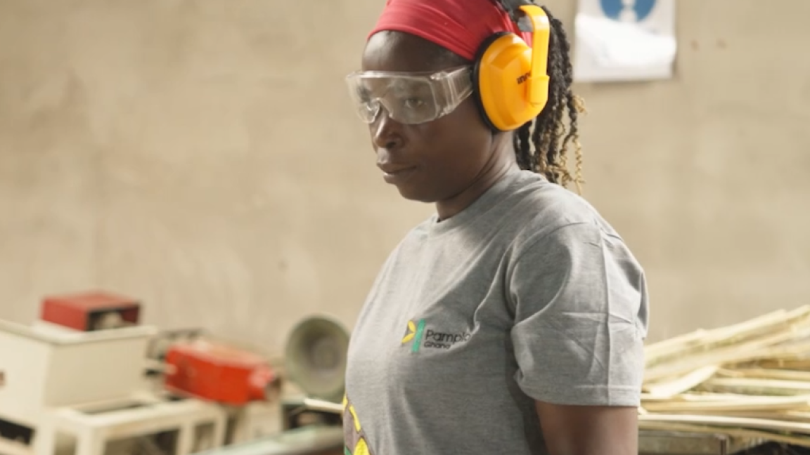 Eine dunkelhäutige Frau mit Schutzbrille und Ohrschützern steht in einer Werkstatt