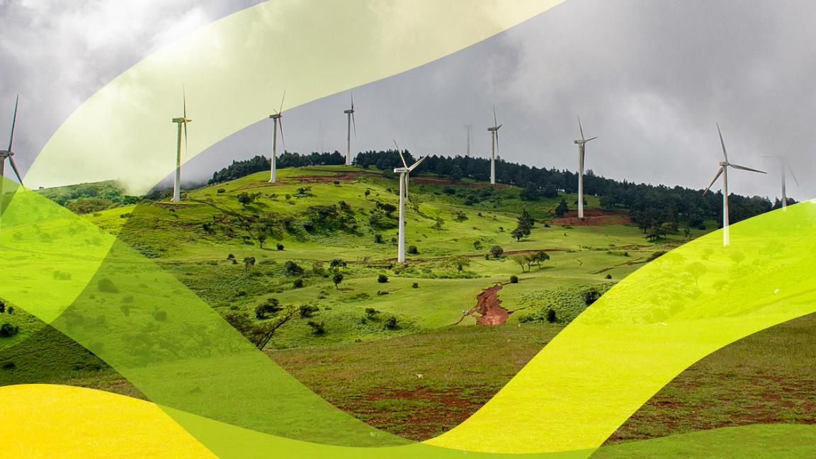 Wind turbines on a green hill under a cloudy sky.