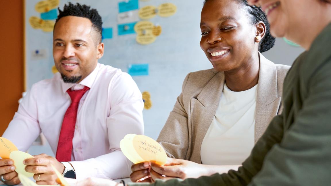 Two women and a man sit at a table, each holding some index cards.