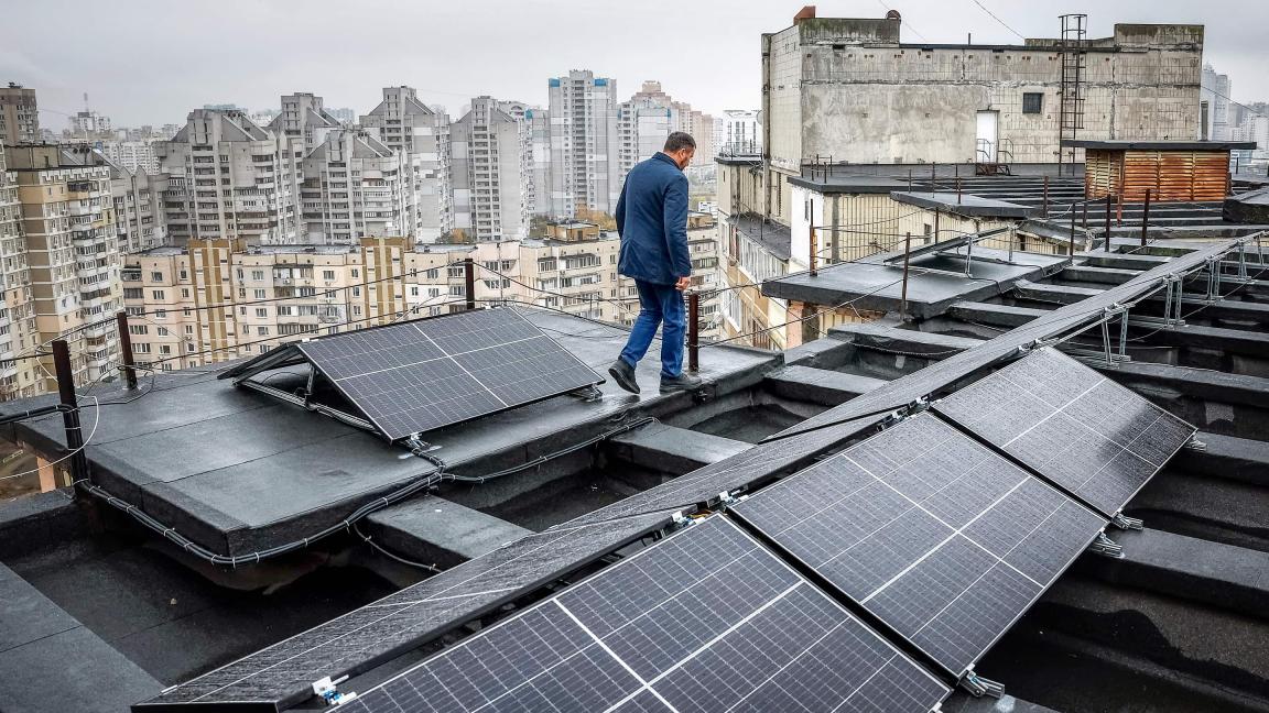 Ein Mann läuft über ein Flachdach mit installierten Solarpanels, im Hintergrund stehen viele Hochhäuser einer Stadt.