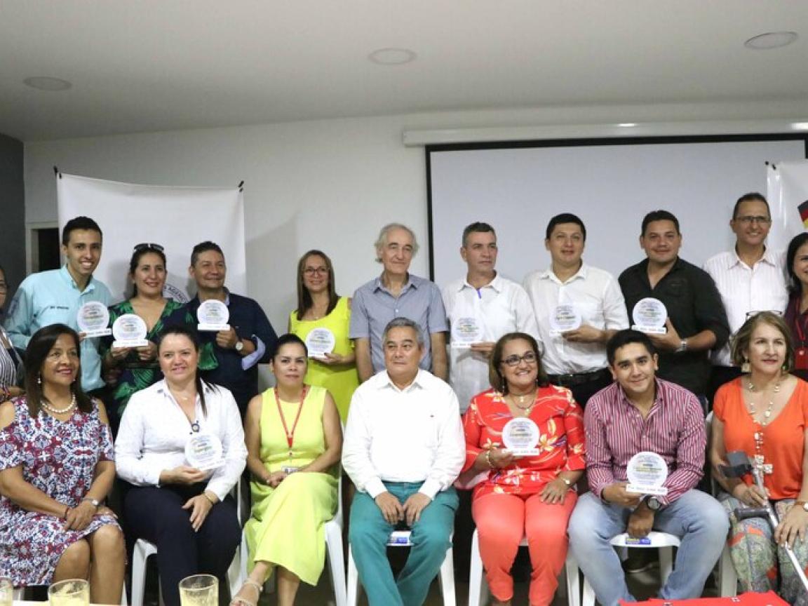 Eine Gruppe Menschen sitzt in zwei Reihen in einem weißen Raum.