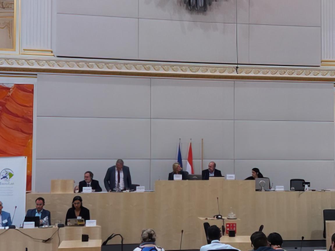 In einem großen Plenarsaal wird eine Konferenz abgehalten.