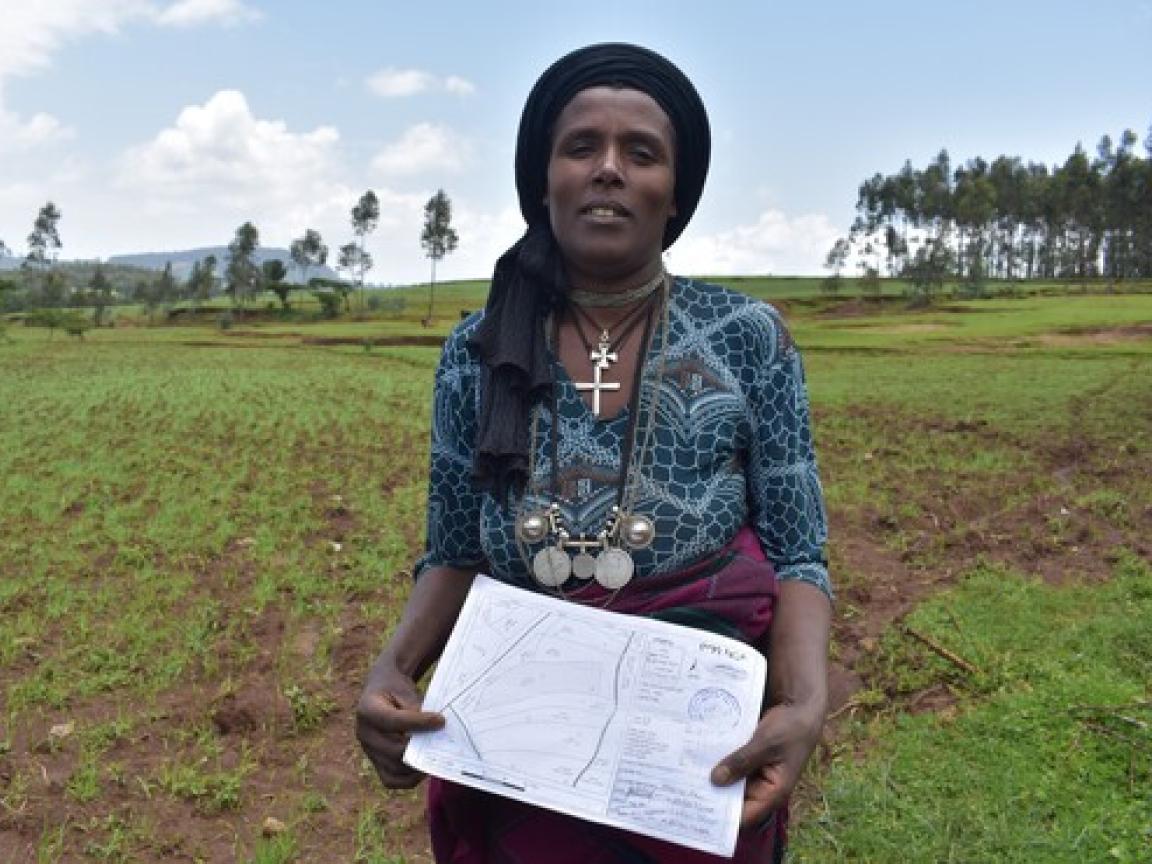 A woman is standing in the middle of a field and holding a paper map in her hands.