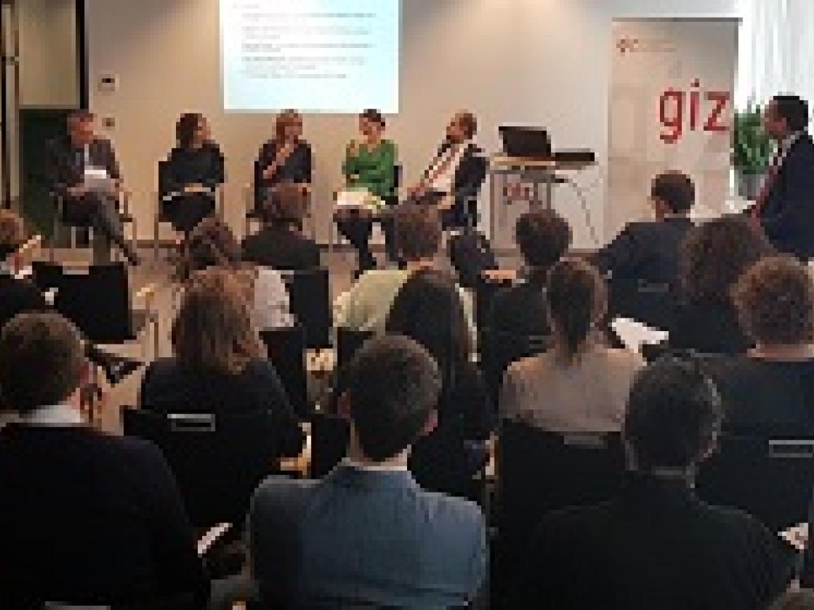 5 Personen sitzen auf Stühlen auf einer Bühne mit Publikum