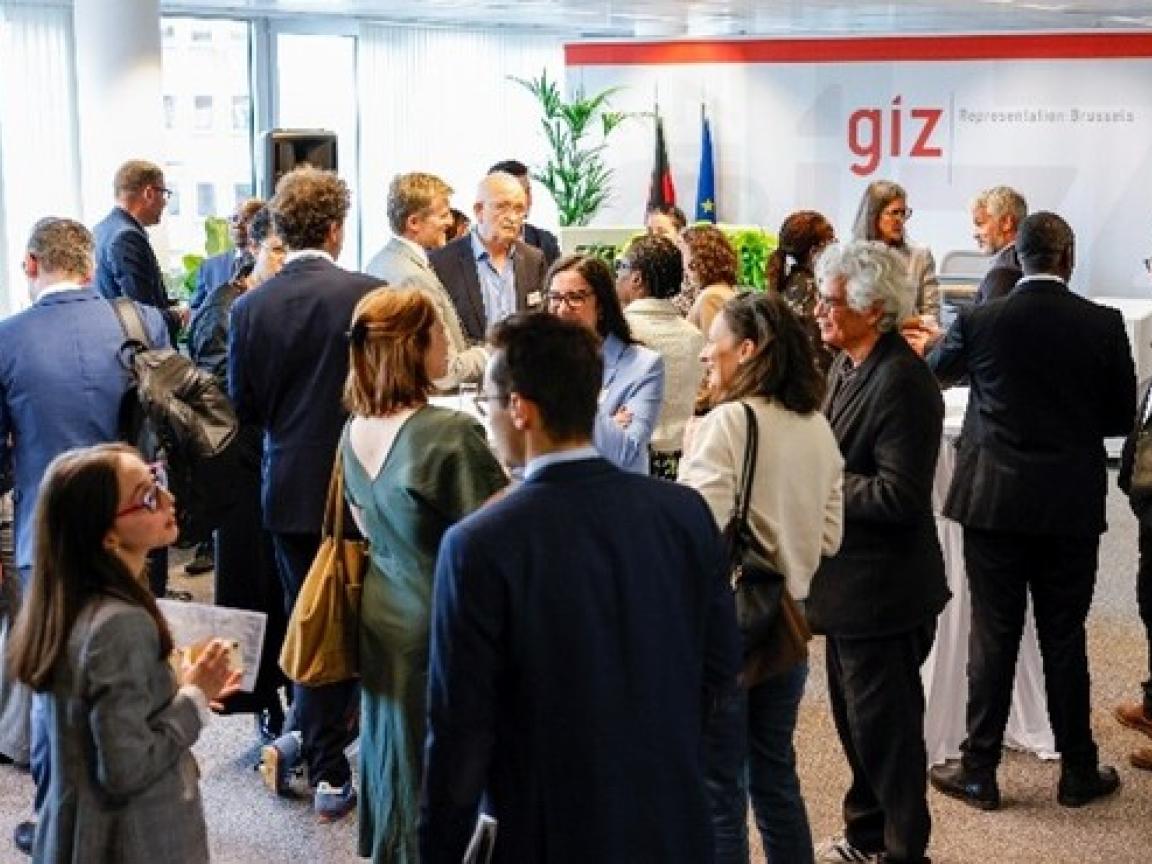 Viele Menschen stehen verteilt in einem Raum. Hinten an der rechten Wand steht "GIZ Representation Brussels"