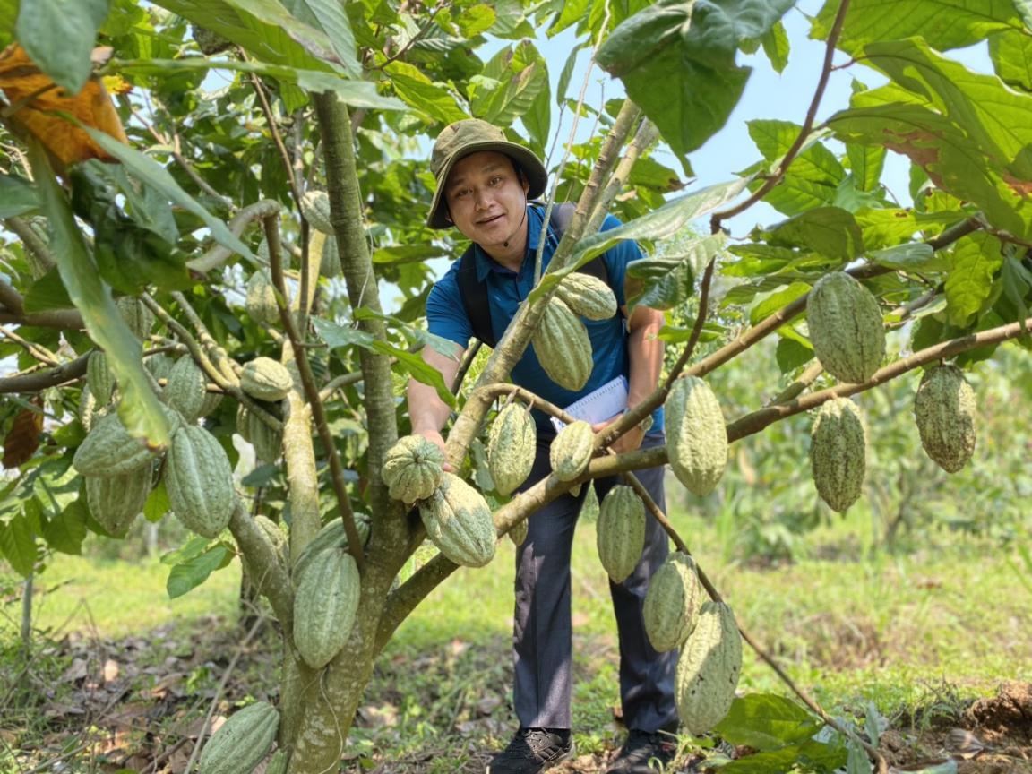 Ein Mann posiert vor einer Kakao-Pflanze.