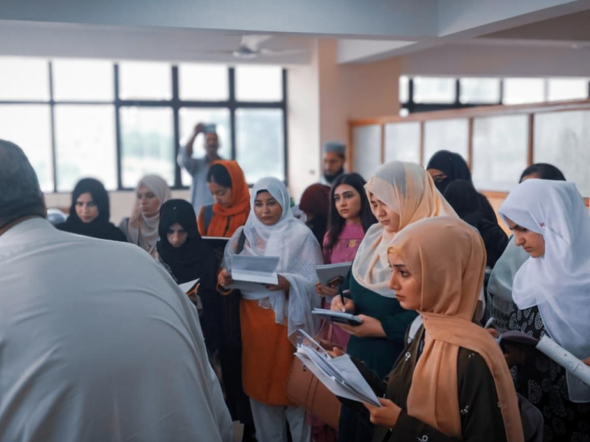 A group of women is standing in front of a control desk and taking notes.