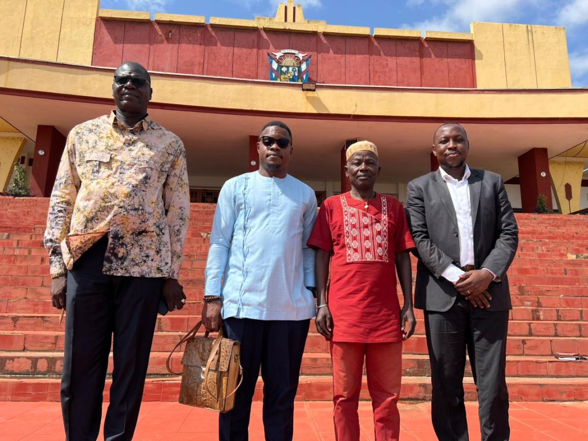 Vier Herren in schicker Kleidung stehen vor einem großen Gebäude.