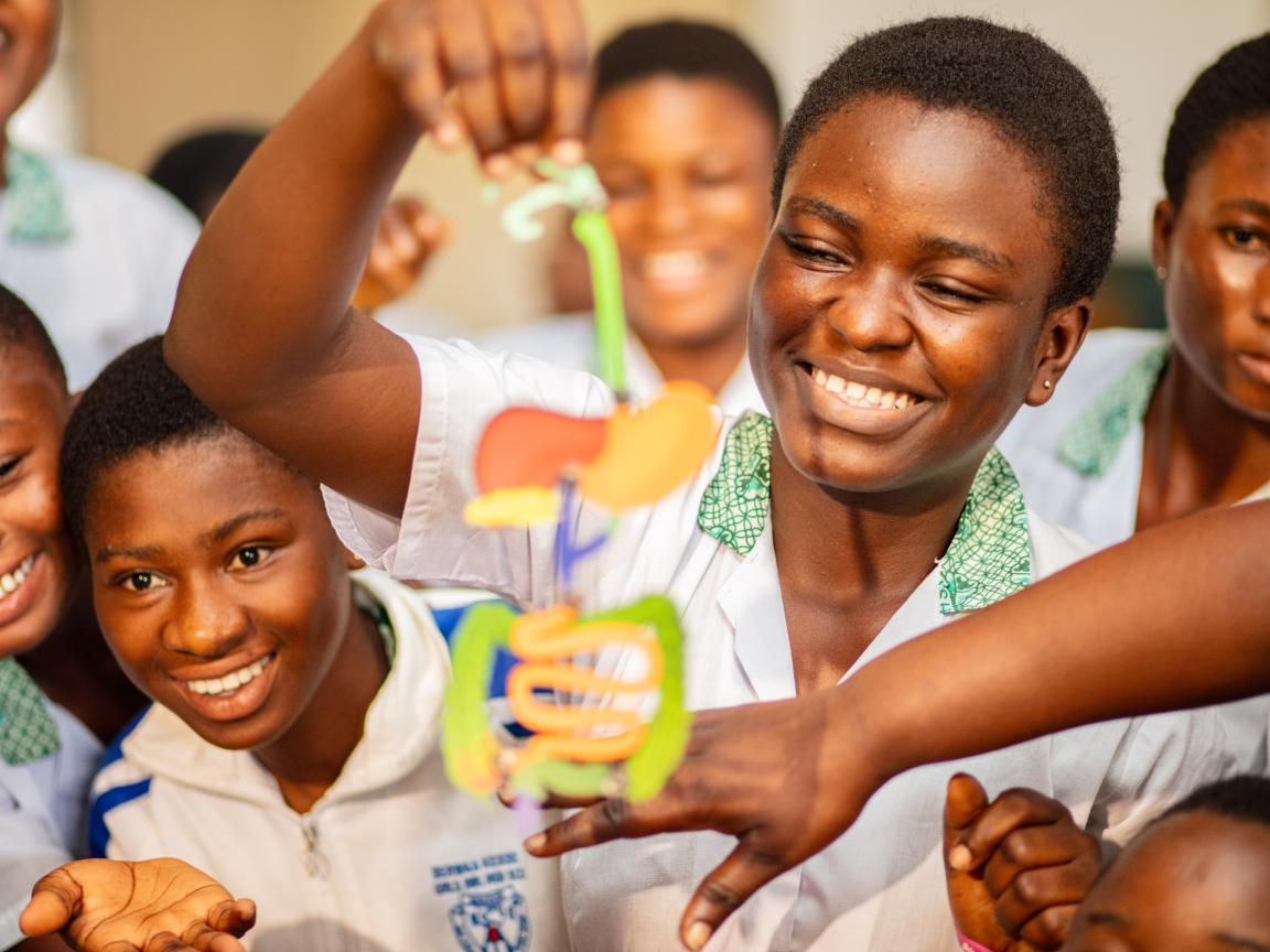 Young women hold up a paper cut-out picture to the camera and smile.