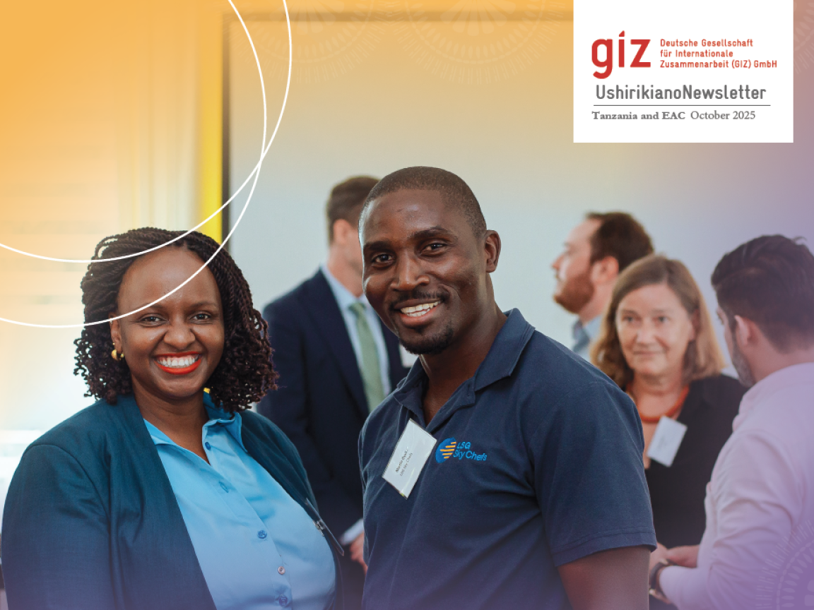 A man and a woman are smiling towards the camera, a few other people are standing in the background.