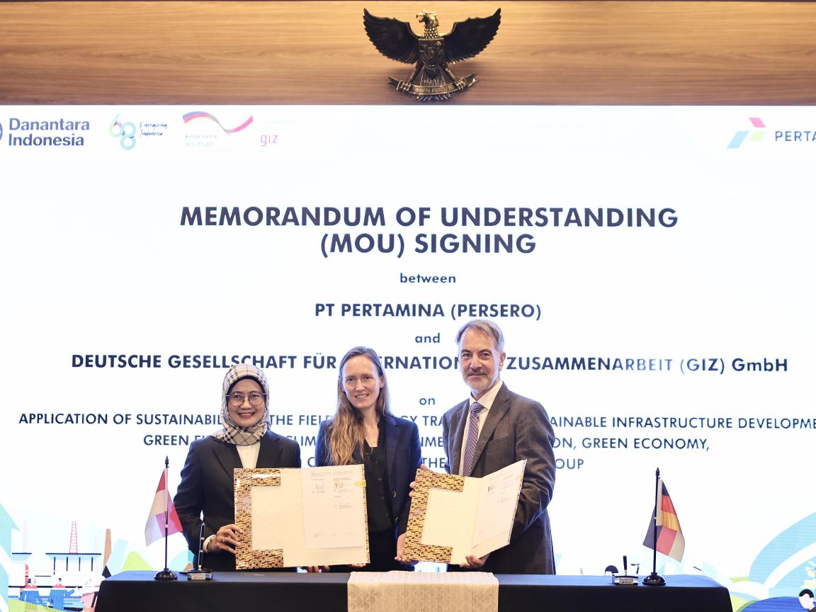 Drei Menschen stehen bei der Unterzeichung eines Memorandum of Understanding vor einer Leinwand. 