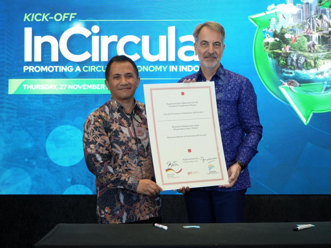 Zwei Männer halten ein großes Dokument in die Höhe, das für Kreislaufwirtschaft in Indonesien steht.