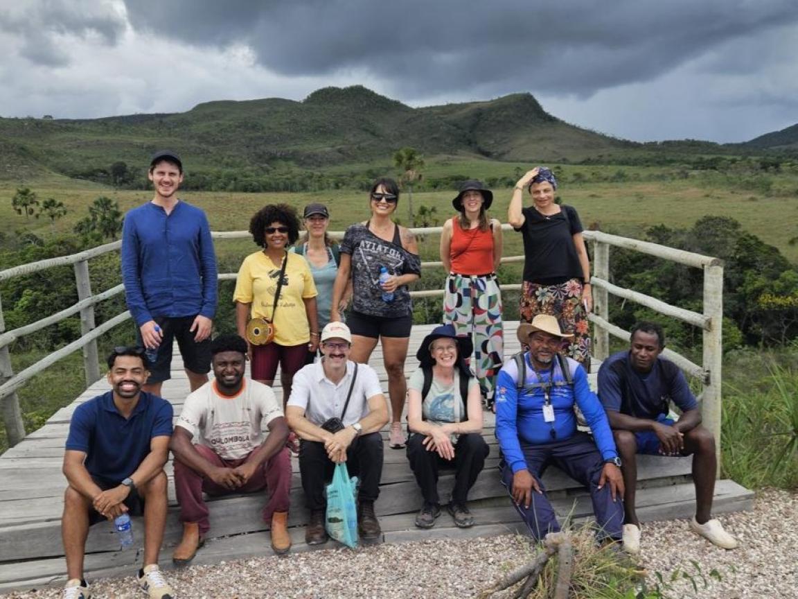 Eine Gruppe von Menschen ist auf einer Holzplattform inmitten grüner Hügel und Wiesen.