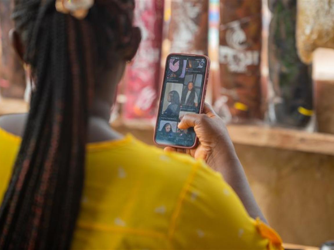 Eine Frau mit Braids sieht sich auf ihrem Handy Flechtfrisuren an. 