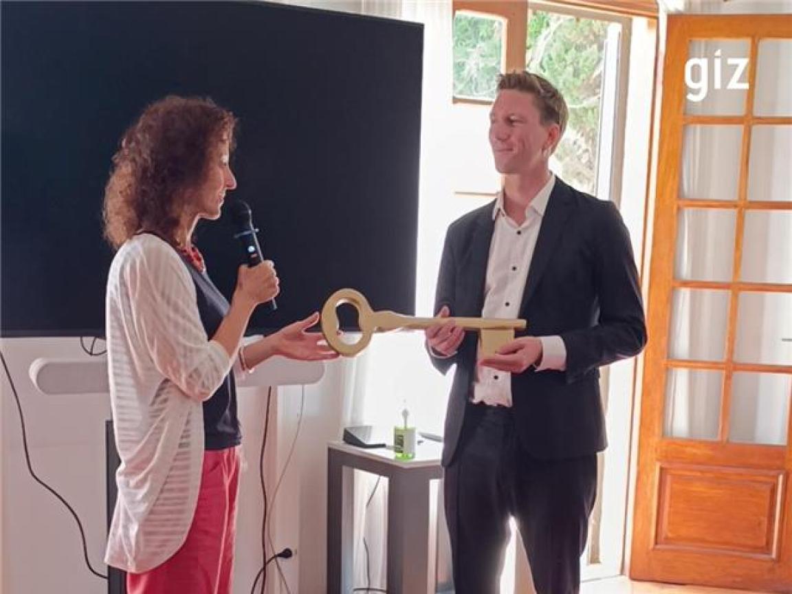 Ein Mann übergibt einer Frau einen symbolisch großen Schlüssel.