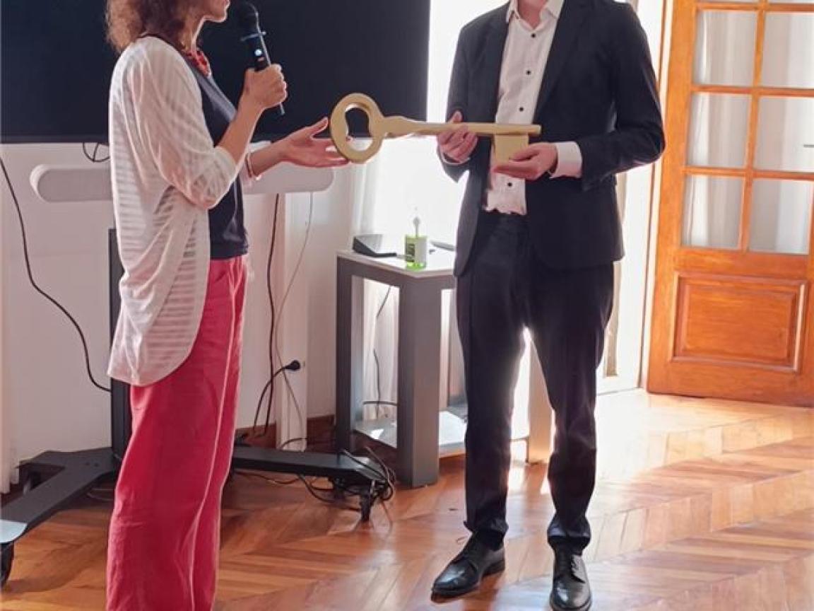 Ein Mann übergibt einer Frau einen symbolisch großen Schlüssel.