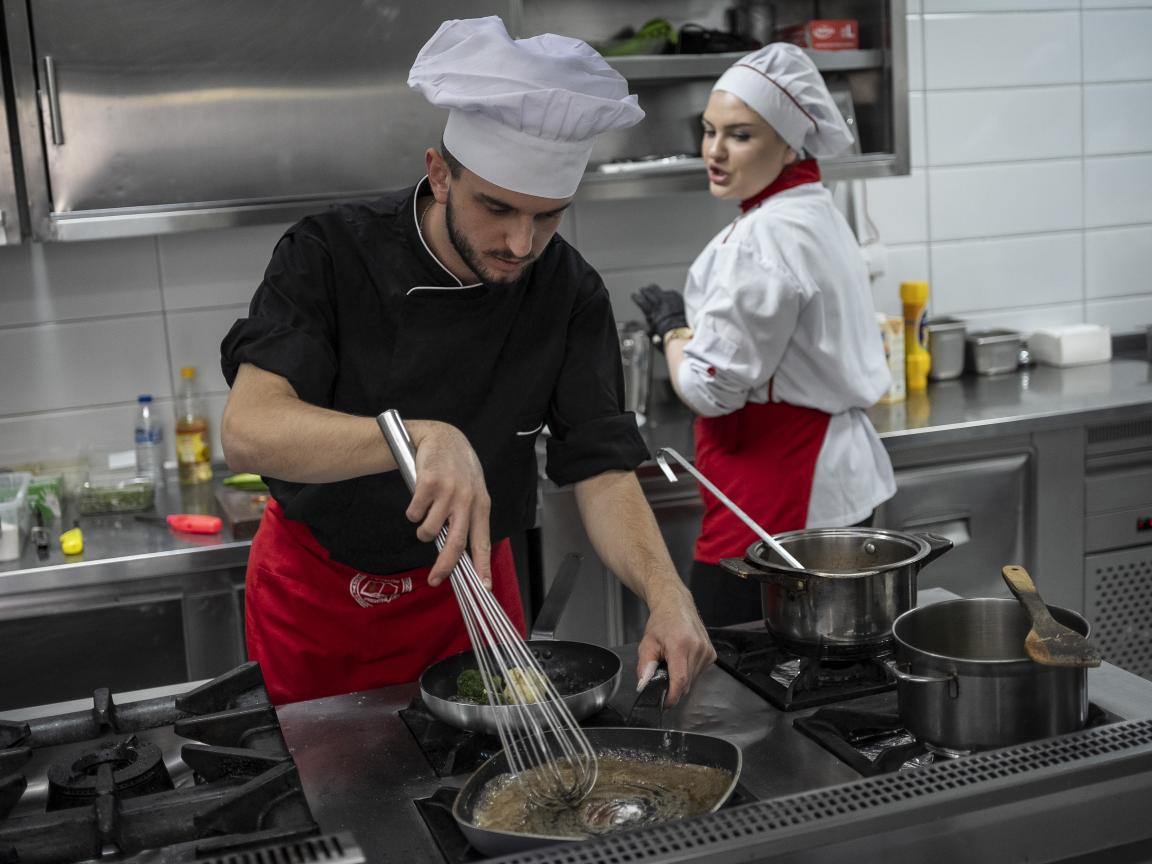 Two VET students are cooking in a professional kitchen.