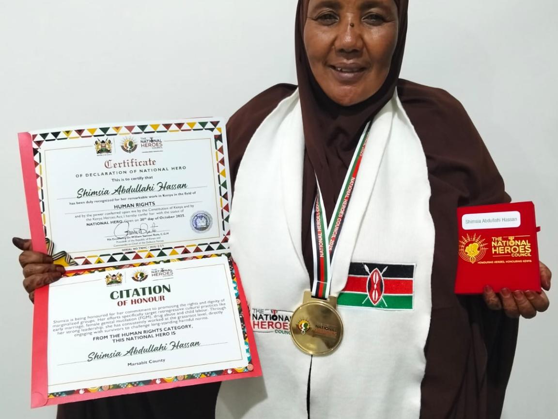 A Kenian woman is displaying a certificate and a medal.
