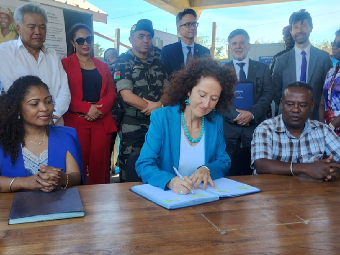 Drei Personen sitzen an einem Tisch und unterzeichnen ein Abkommen. 