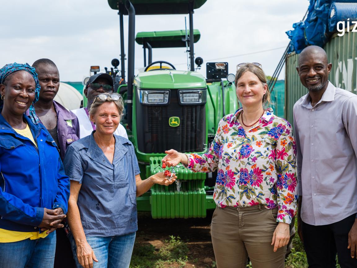 Fünf Menschen bei der symbolischen Schlüsselübergabe eines Traktors.