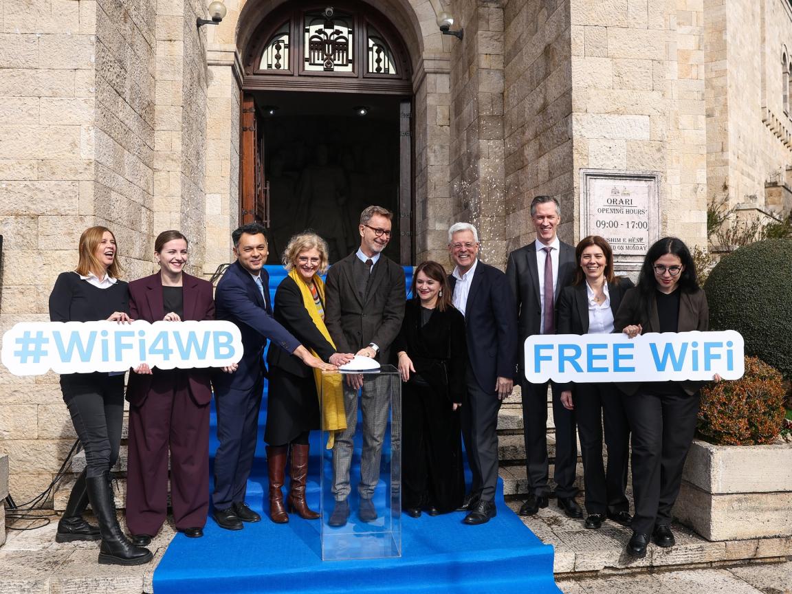 A group of people in official attire are holding up signs that read #FreeWifi and #Wifi4WB.
