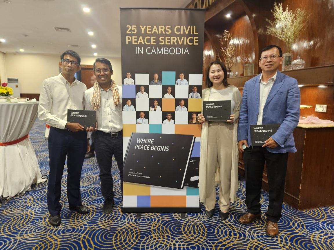 Four people are standing in a hotel lobby where 25 years of Civil Peace Service in Cambodia are being celebrated.