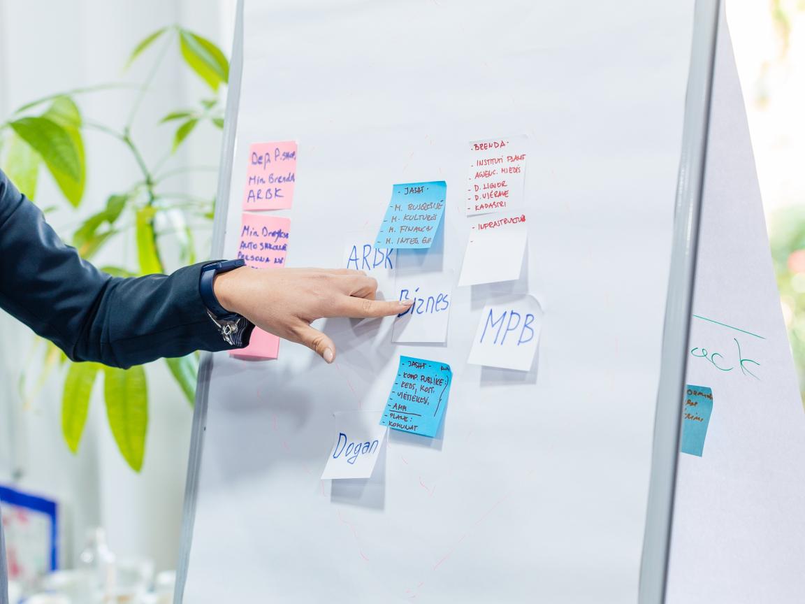 A person is standing in front of a flip chart and pointing at some sticky notes.