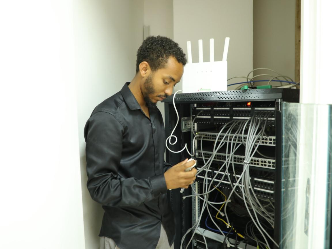 A man in a black button-down shirt is testing cable nodes of a server in a room of Africom Technologies.
