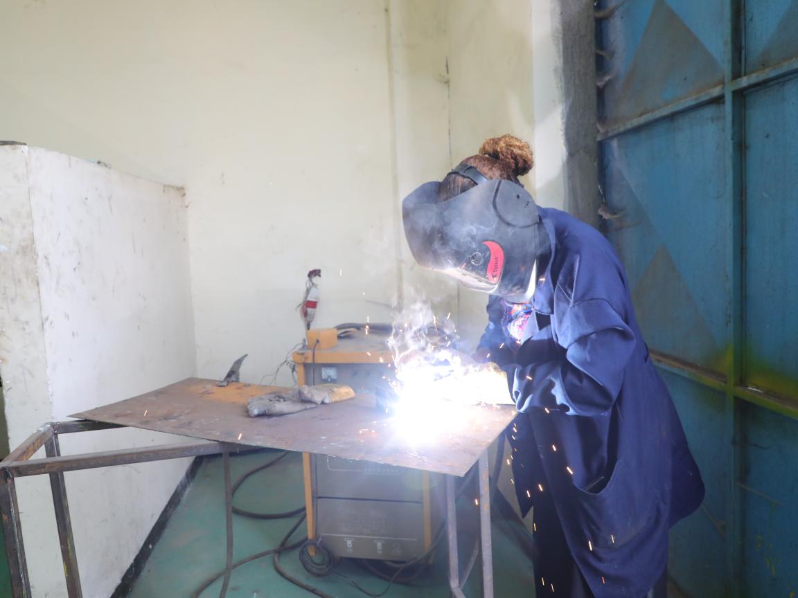 Eine Person in Arbeitskleidung schweißt in einer Arbeitshalle.