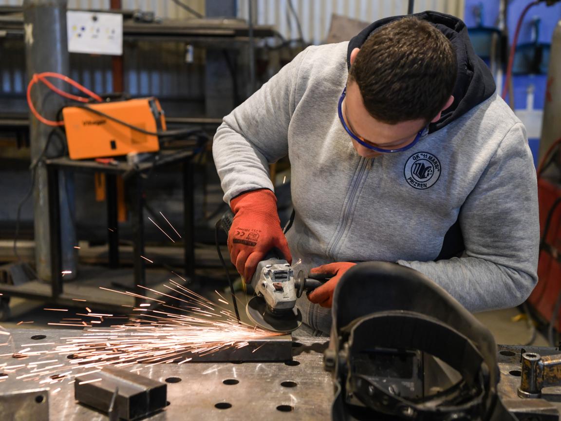 A young tradesman is grinding a piece of metal with a machine.