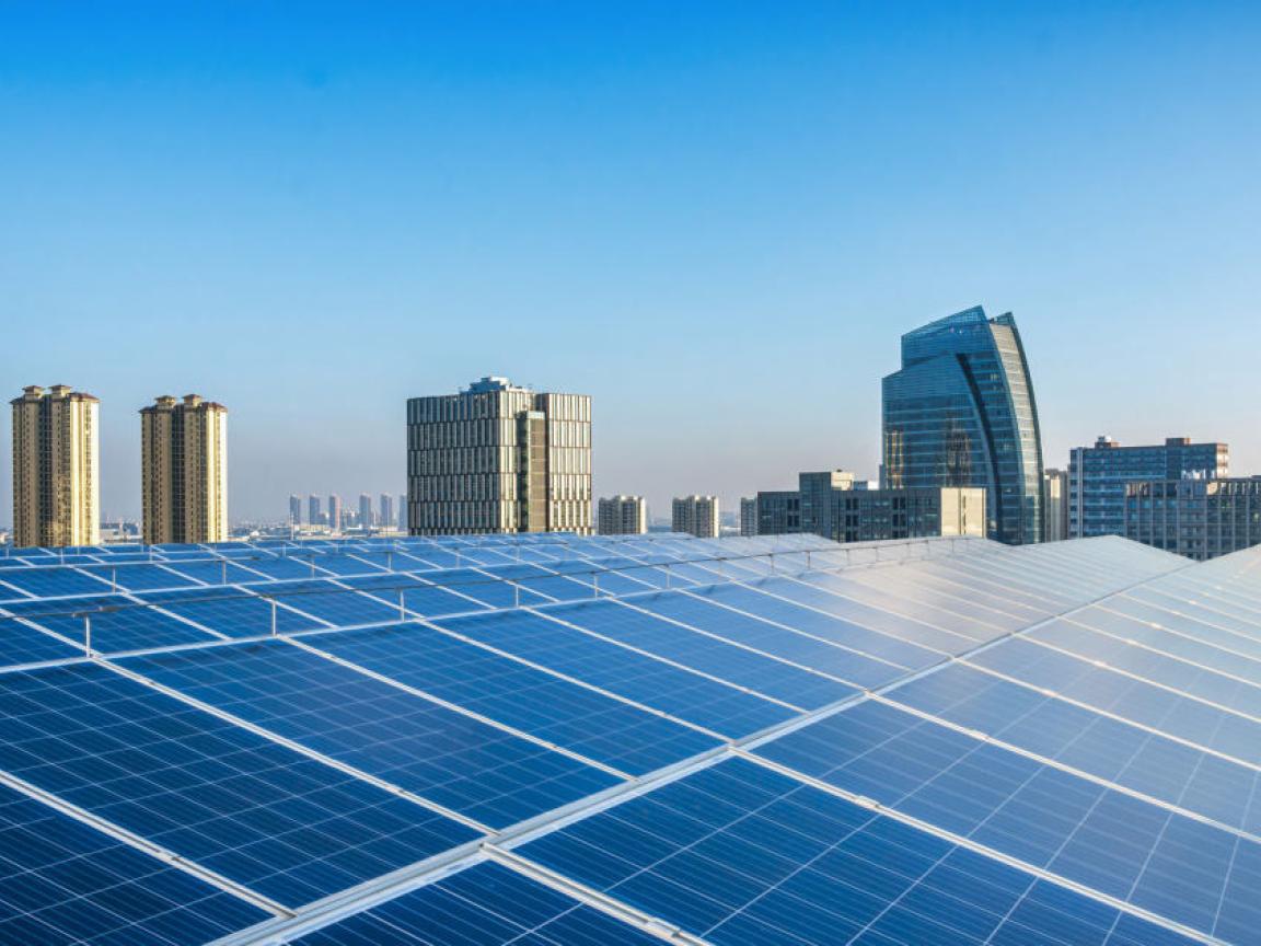 Rooftop solar photovoltaic panels installed on a modern urban building, with a city skyline in the background