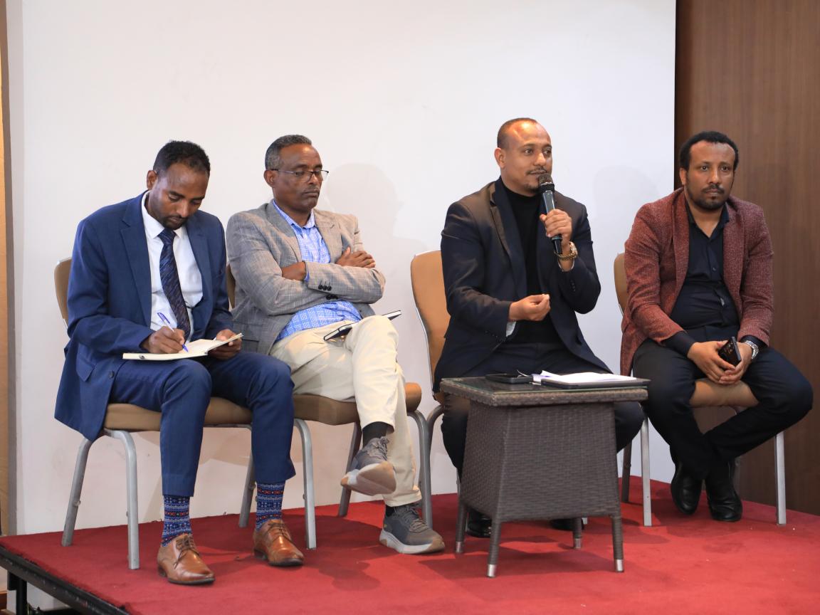 A group of panelists with one of them holding a mic and speaking 