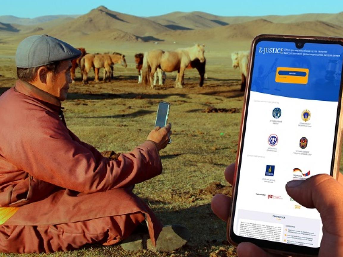 Ein Mann sitzt in der Steppe und hält ein Smartphone in der Hand.