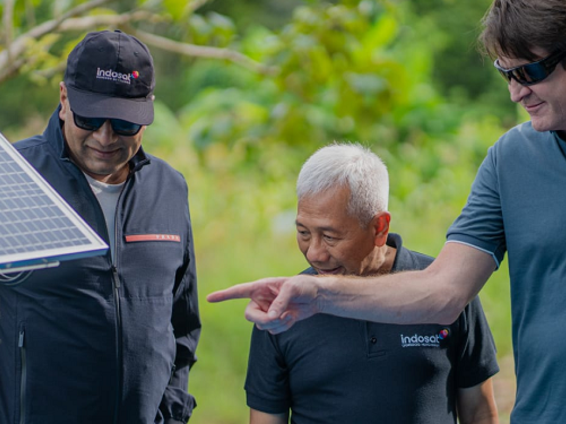 Drei Männer schauen auf ein Solarpanel, das in der Natur steht.