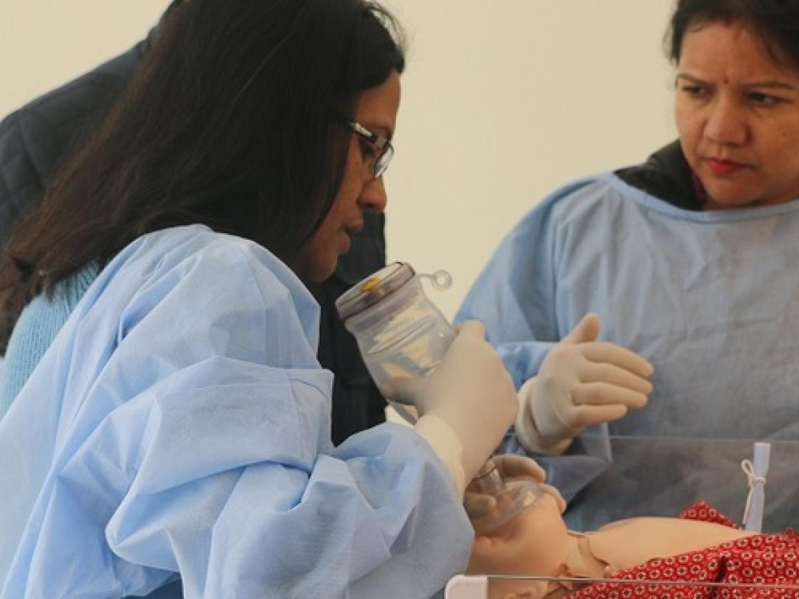 Zwei Frauen und ein Mann stehen um eine Simulationsbeatmung herum.