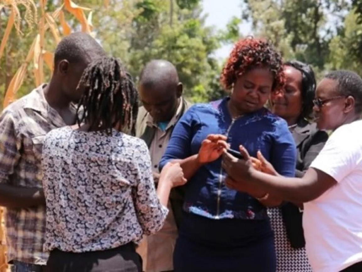 Sechs Menschen stehen eng zusammen und schauen auf ein Smartphone.