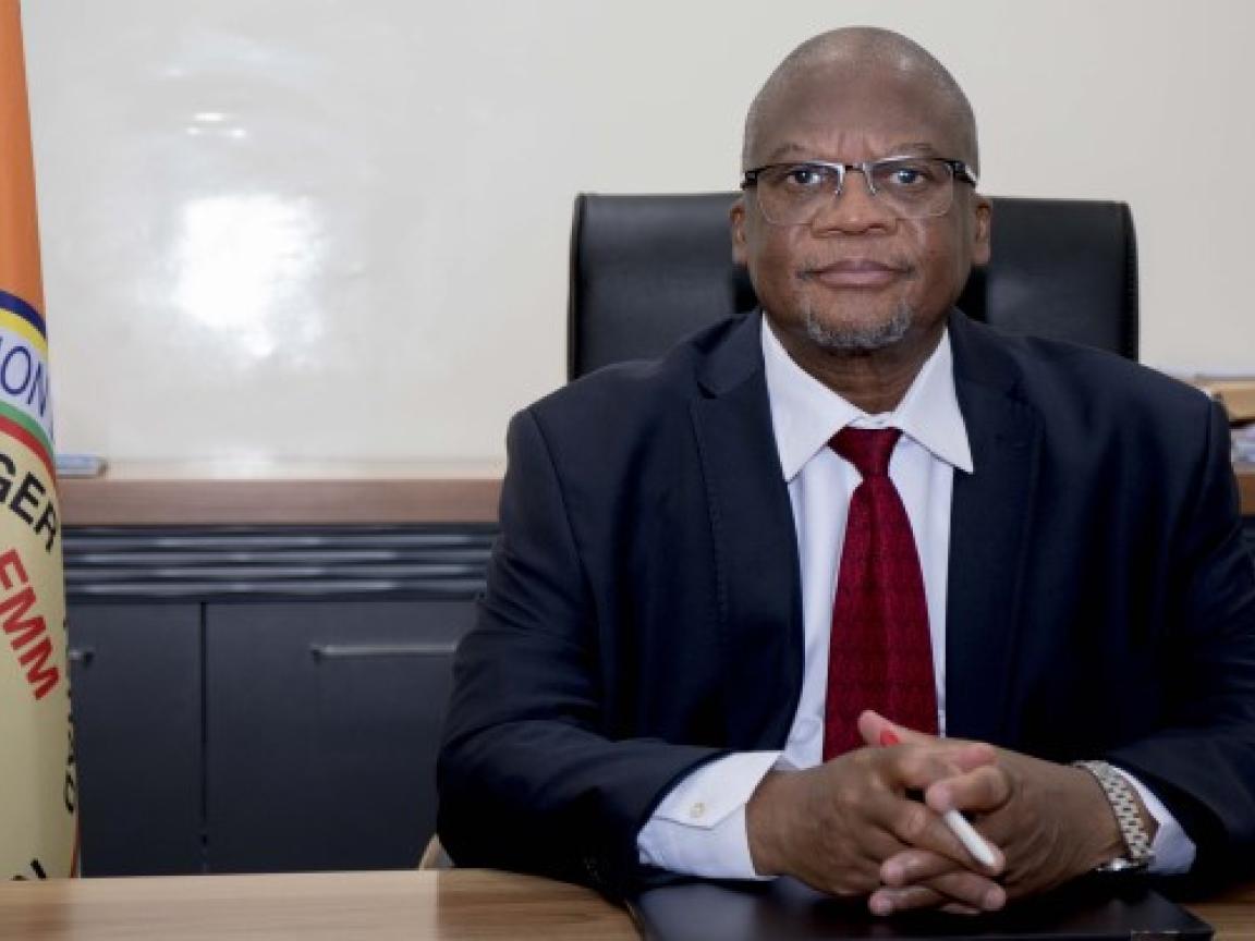 Ein Mann (Mamman Nuhu) sitzt an einem Schreibtisch und schaut ernst in die Kamera.