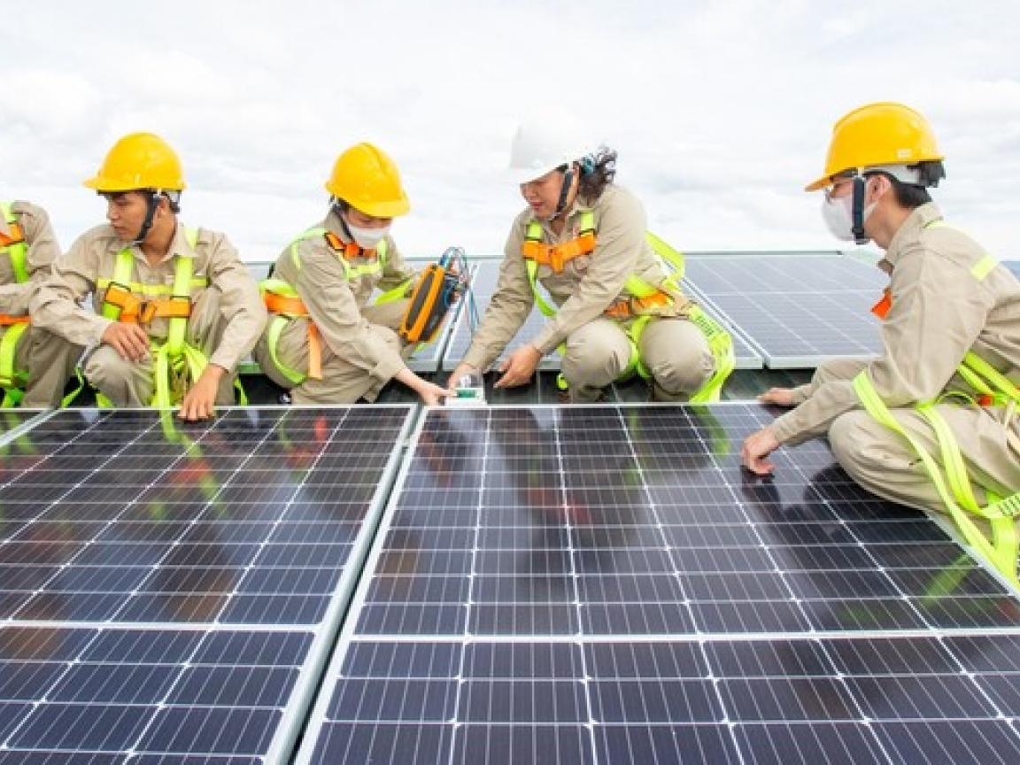 Junge Leute in Arbeitskleidung montieren Solarzellen auf einem Dach.