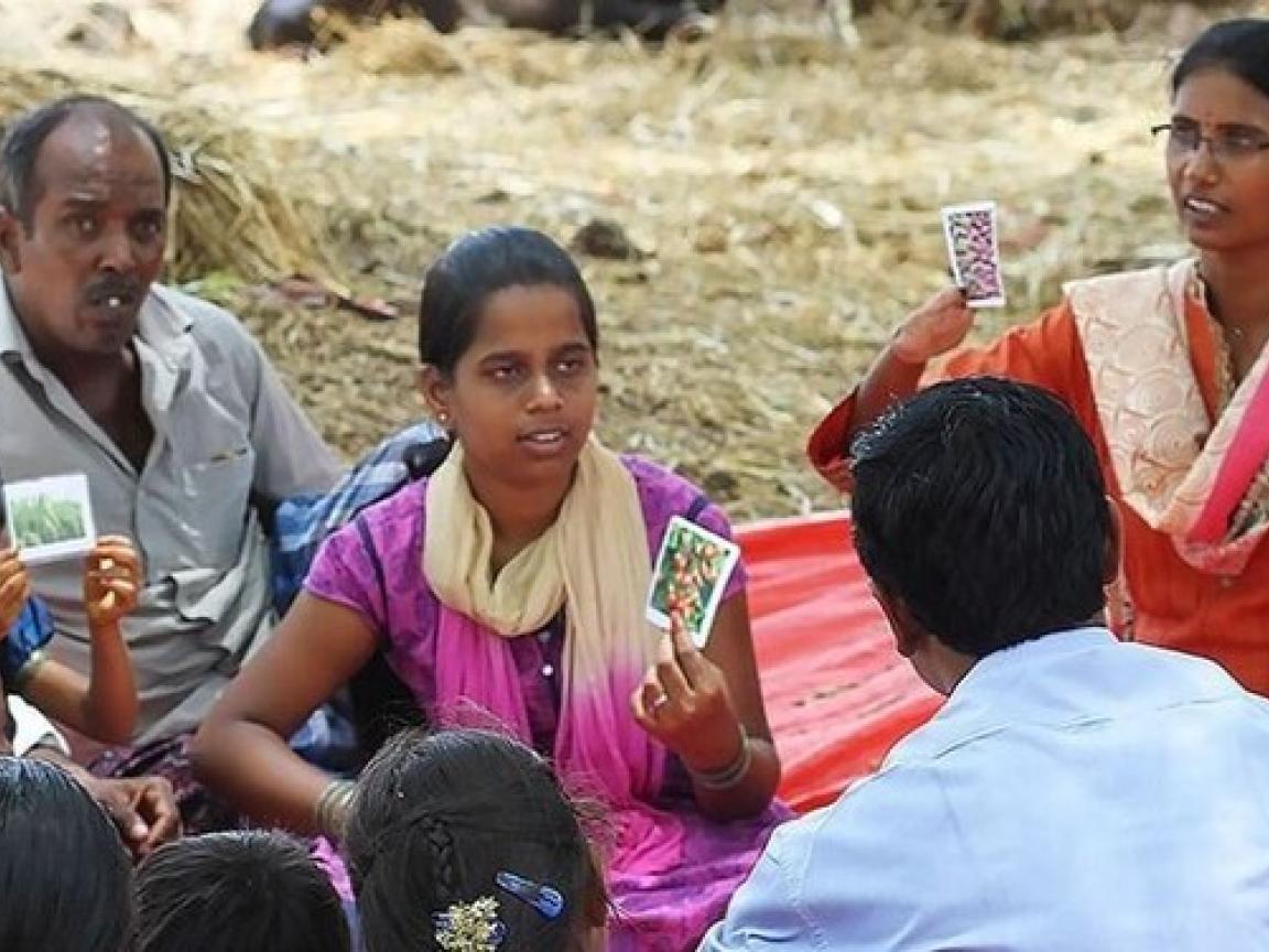 Eine Gruppe von Menschen sitzt im Freien auf einer roten Plane und spielt Karten.