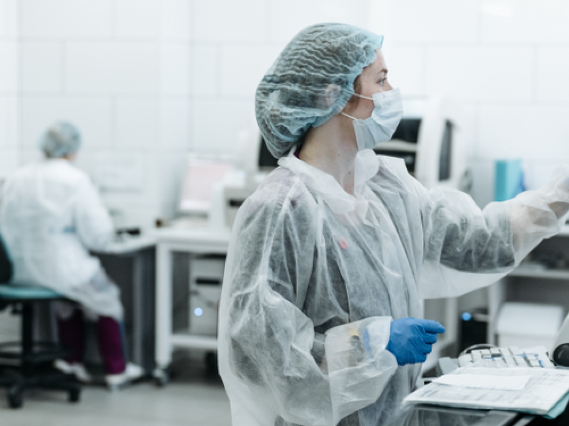 Eine Ärztin in Laborkleidung tippt auf einen Monitor.