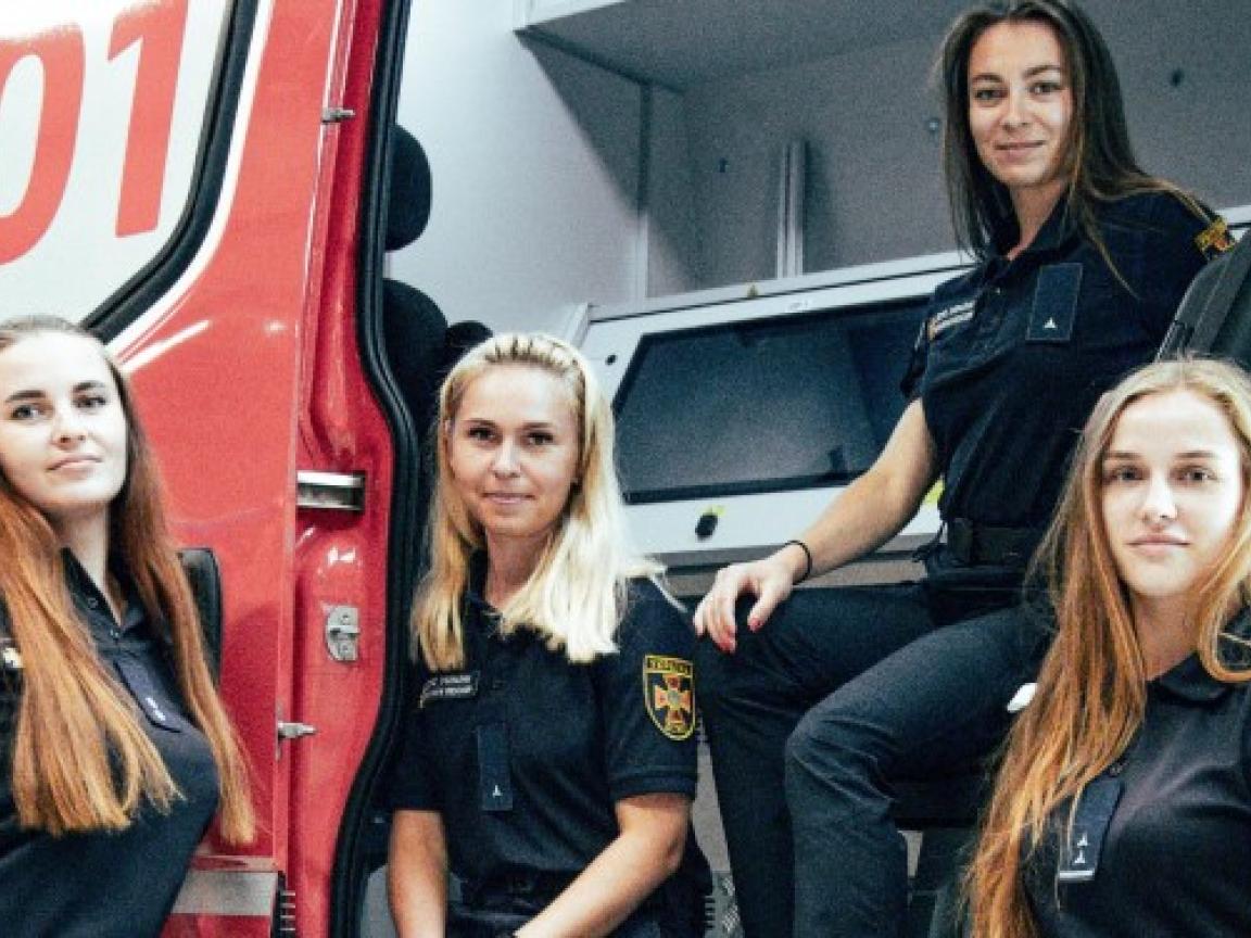 Vier Feuerwehfrauen stehen und sitzen an der Tür eines Feuerwehrautos.