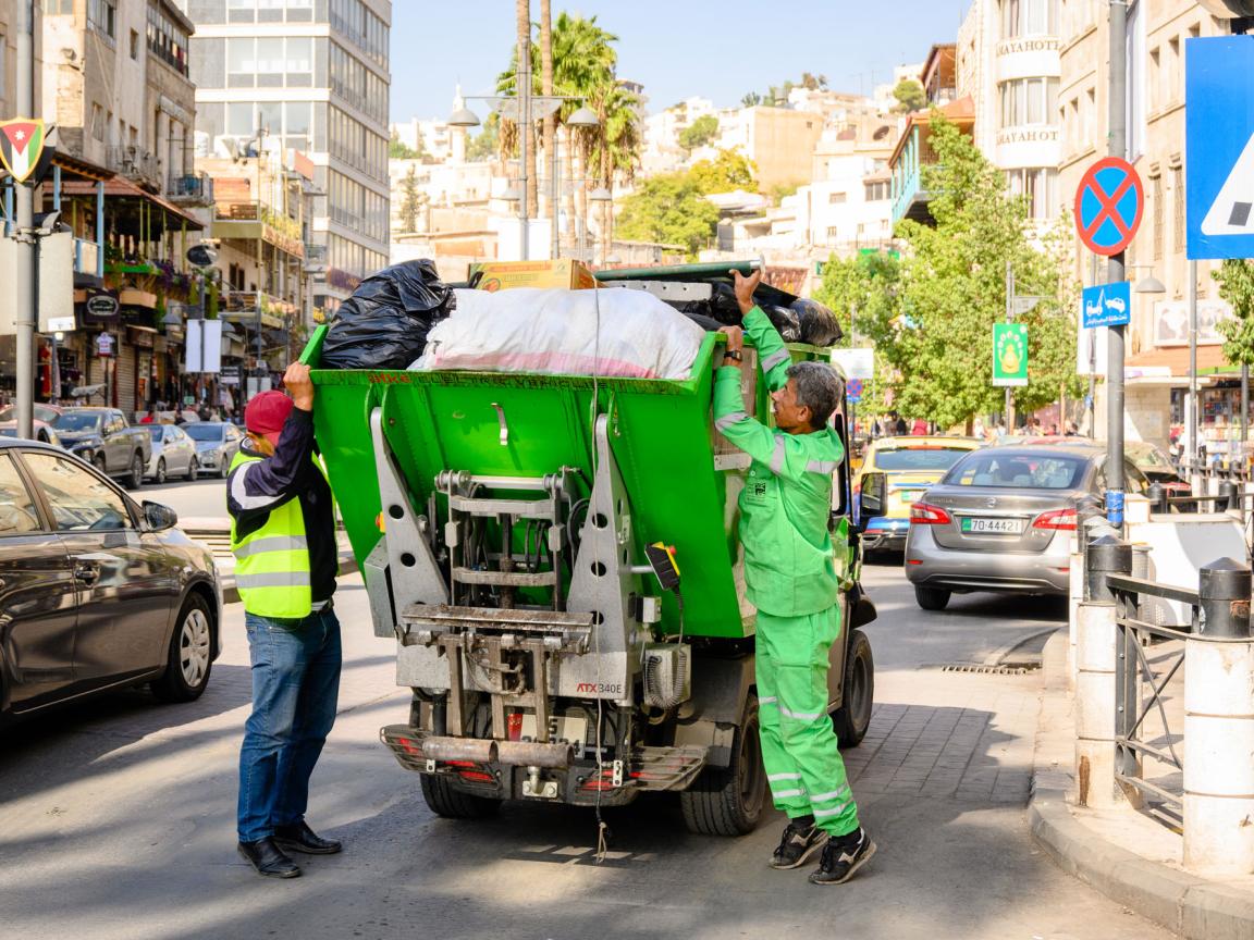 Men loading rubbish into a small rubbish truck