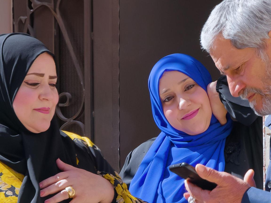Zwei Frauen mit Kopftuch und ein Mann am Handy