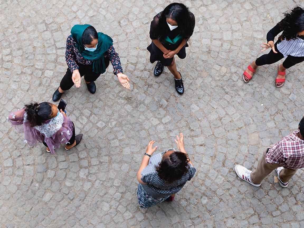 A photograph of young Ethiopian women and girls, as well as one man, standing on a paved surface and engaged in lively conversation. The individuals' clothing varies, with visible details such as a scarf and different patterns on their tops.