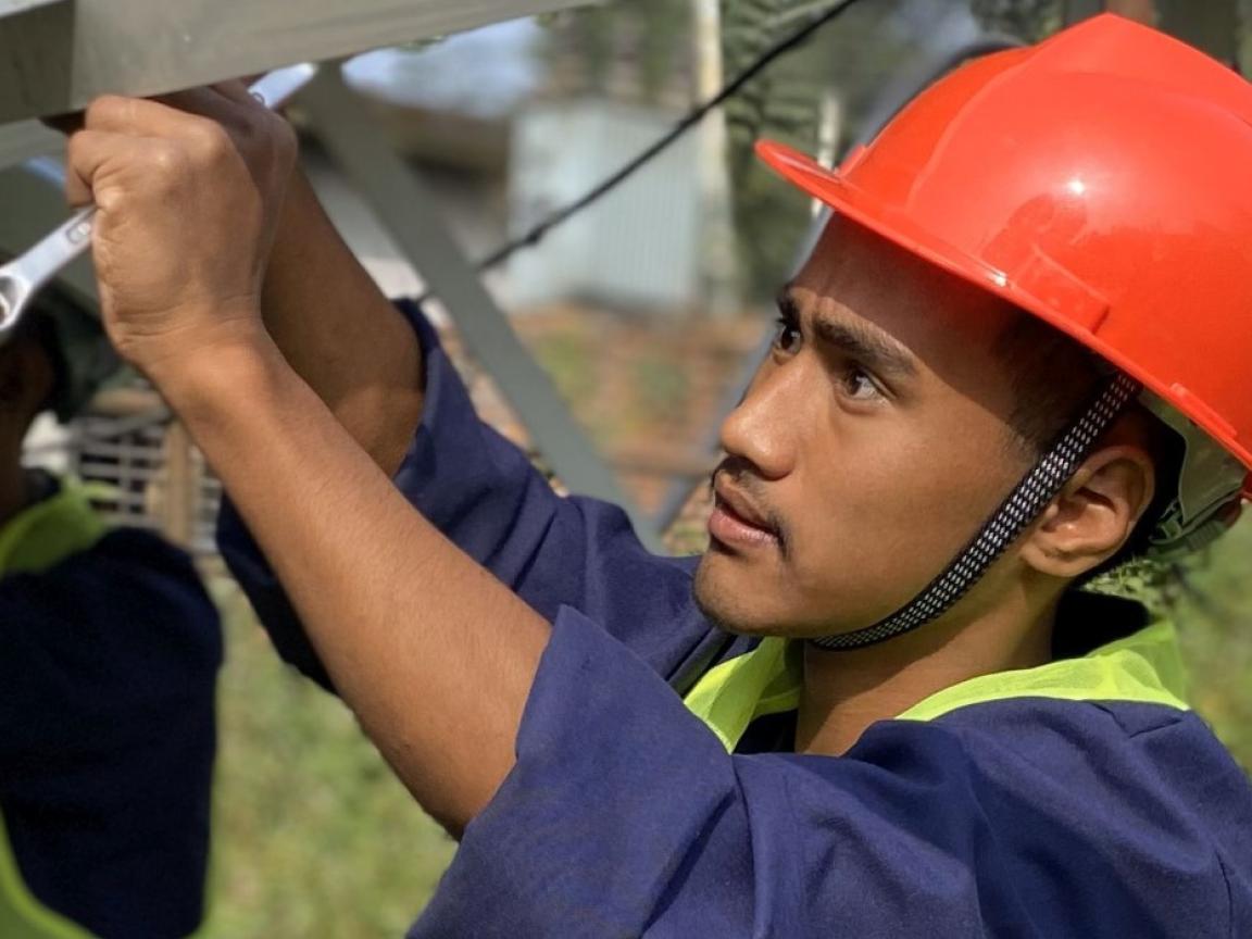 Ein Mann mit rotem Schutzhelm blickt konzentriert auf eine Metallkonstruktion und hält einen Schraubschlüssel in der Hand.