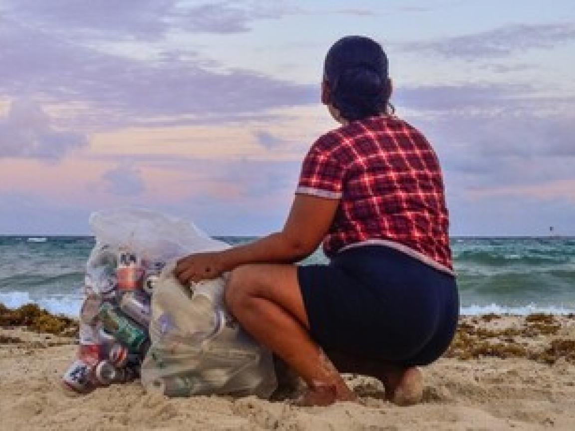 A woman sits on a beach in Mexico next to two full bags of trash she collected earlier.