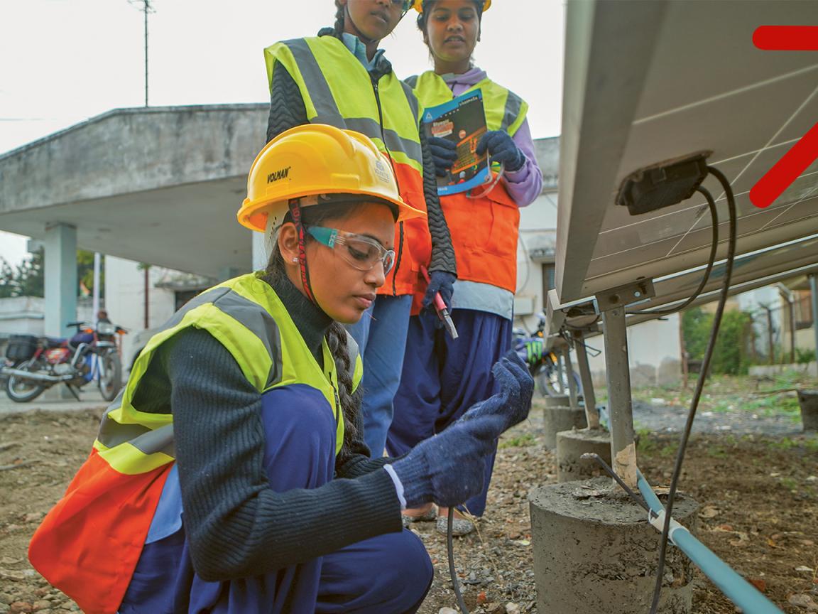 Eine Frau in Arbeitsbekleidung überprüft Kabelverbindungen eines Solarmoduls. 