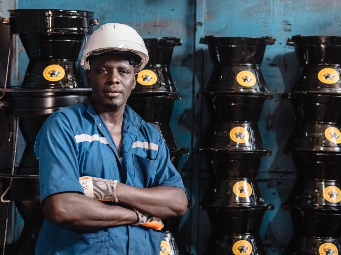 Ein Mann mit einem weißen Helm steht vor einer Wand, an der Herde zum Kochen aufgetürmt sind. 