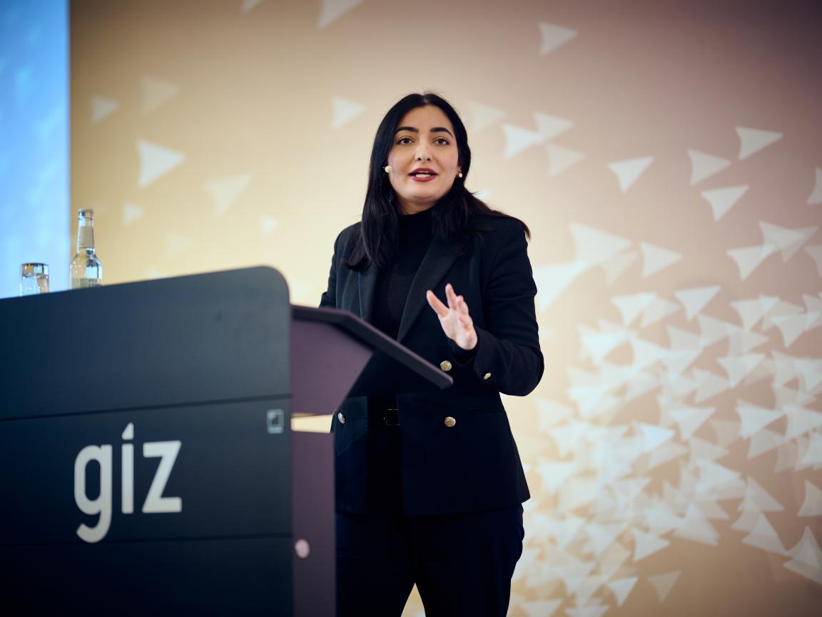 A woman with dark hair is standing behind a lectern.