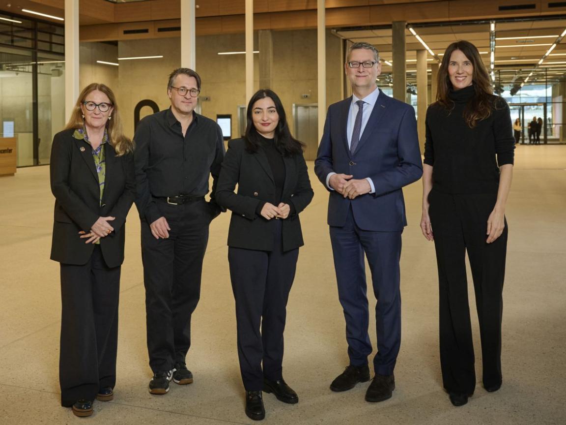 Fünf Personen in Businesskleidung stehen lächelnd in einem großen Raum